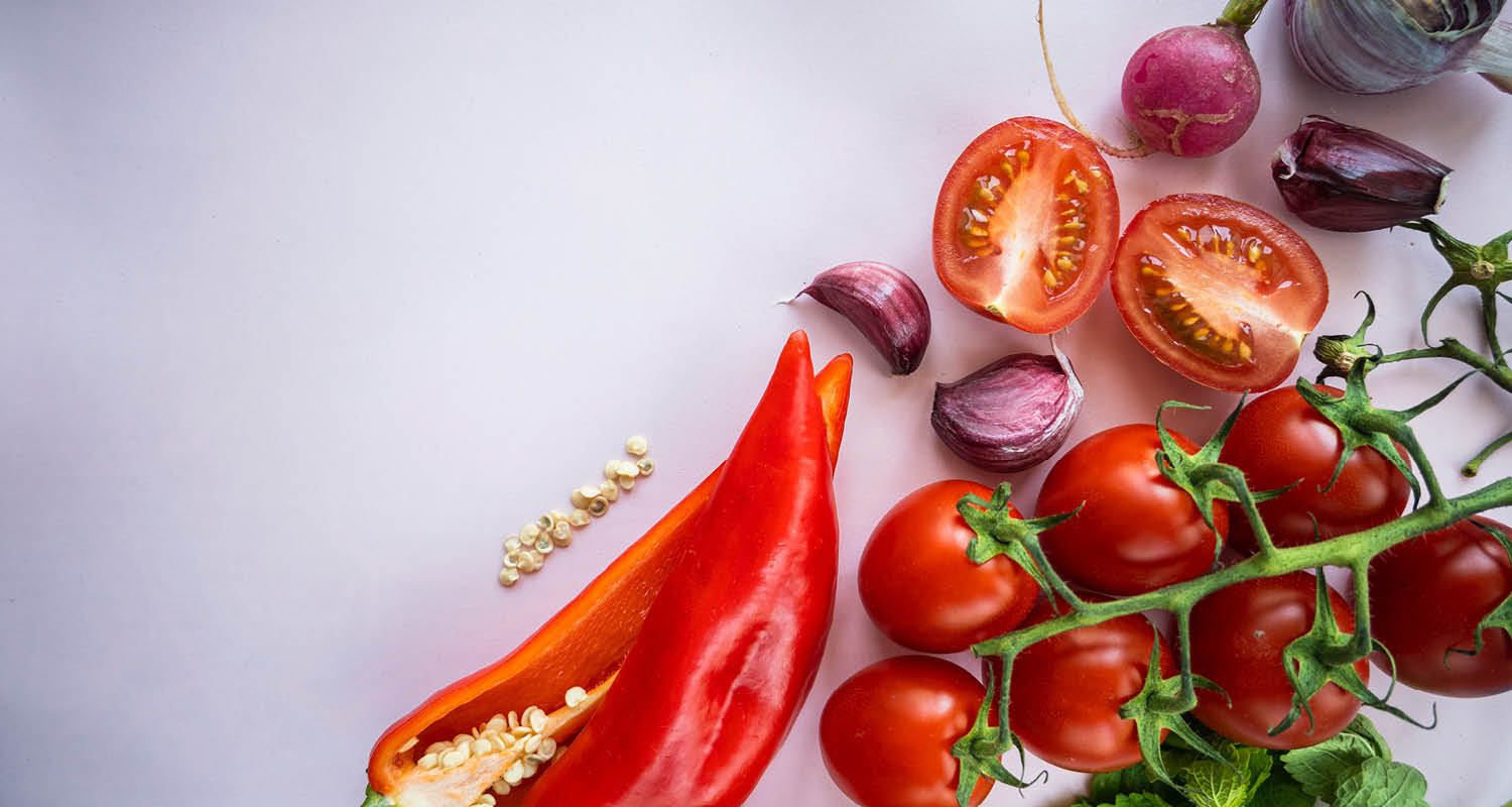 Frisches Gemüse: Tomaten, Paprika, Radieschen und Knoblauch auf hellem Untergrund.