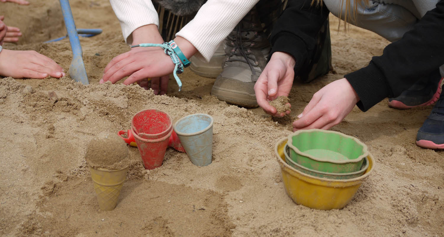 Kinderhände spielen im Sand mit bunten Förmchen und Bechern