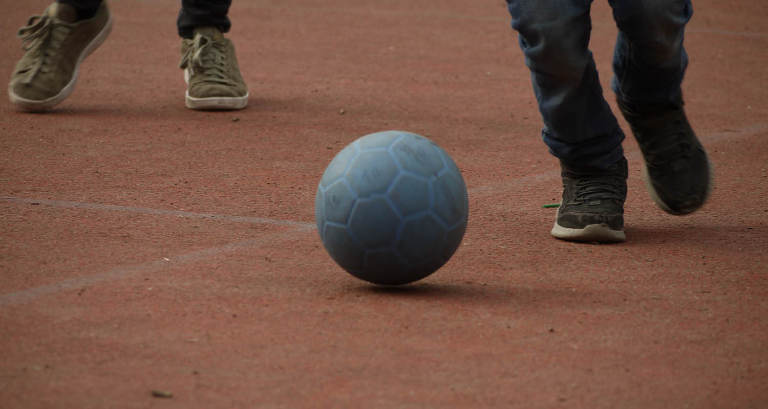 ein Ball auf einem Sportplatz mit Füßen die hinterherlaufen