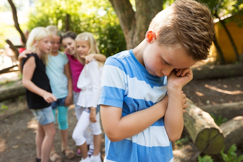Kind steht traurig abgewandt von einer Gruppe Kinder in einem Gartenr
