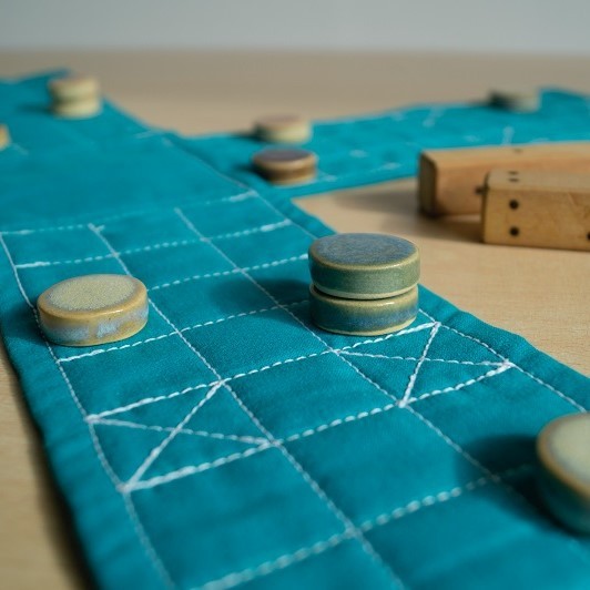 Spielsteine aus Holz liegen auf einem blauem Stoff, welcher als Spielfläche dient