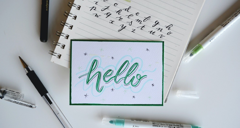 Handlettering Karte mit Aufschrift Hello auf einem Block mit Stiften daneben