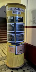 Runde gelbe Informationssäule mit mehreren Aushängen